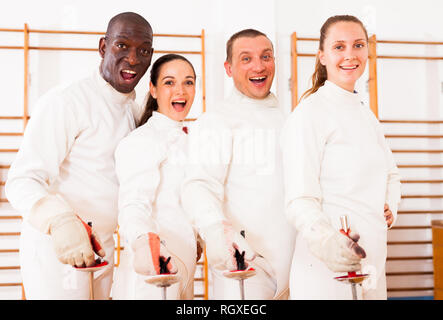 Gruppe positiver Fechter stehen mit Folien zusammen an fechten Training Stockfoto