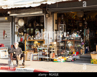 Die Altstadt von Jaffa, Tel Aviv, Israel - 23 Dezember, 2018: eine alte Anbieter in einem Sessel sitzend vor seinem Antiquitätenladen in den berühmten Flohmarkt in der Altstadt von Jaffa. Stockfoto