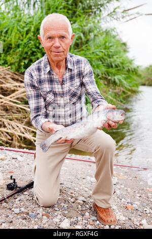 Portrait von zufriedenen Jahren Fischer mit frischen Forellen am Flußufer auf Sommer Stockfoto