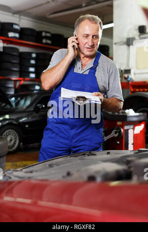 Professionelle Mechaniker in der Werkstatt, um am Telefon für sie notwendige Ersatzteile Stockfoto