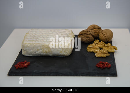 Tomino Käse auf Schwarz Tischdecke mit kleinen roten Beeren und Nüssen dekoriert. Stockfoto