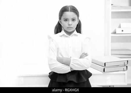 Smart Blick. Kind Mädchen trägt uniform Stehen mit verschränkten Armen auf der Brust. Schulmädchen smart Kind schwerwiegende innen weiß Hintergrund. Mädchen ernst über Wissen und Bildung in der Schule. Stockfoto