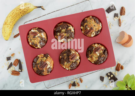 Frisch gebackene Banane Haferflocken Pecan und Schokolade Muffins in rotem Silikon Muffin von Overhead in natürlichem Licht schoss Pan. Gesunde und nahrhafte Zwischenmahlzeit. Stockfoto