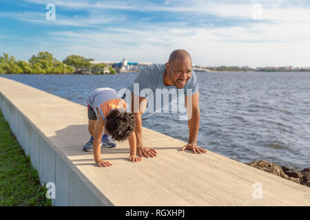 Der junge Vater lehrt seine kleinen Jungen die Bedeutung guter Gesundheit und Bewegung. Mit seinem Sohn wie Liegestütze auf einer ufermauer im Park zu tun. Stockfoto