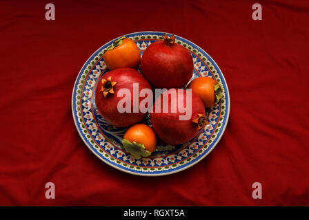 Herbst und Winter Früchte: Granatapfel und Quitte und Dekorative Platte auf rotem Tuch. Stockfoto