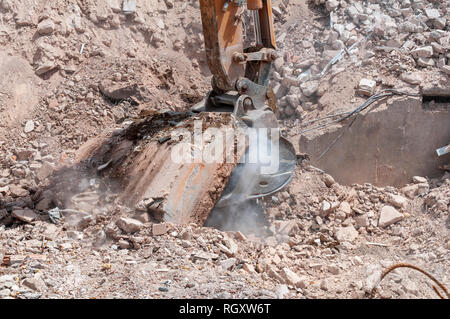 Auf einer Abbruchbaustelle der Schaufel von einem Bagger zieht eine Betonplatte, bleibt das Fundament eines Gebäudes. Stockfoto