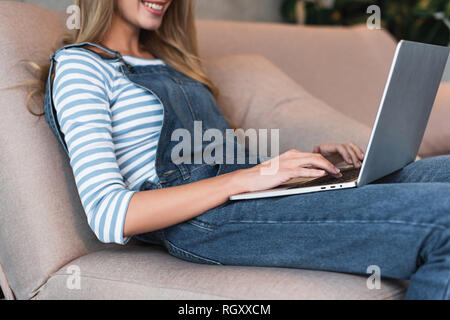 7/8-Ansicht der jungen Frau lächelnd und Tippen auf Laptop Stockfoto