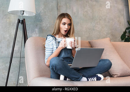 Junge Frau mit Schale in die Hände entsetzt und sitzt mit Laptop Stockfoto