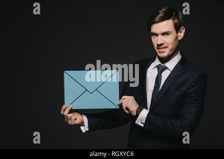 Gut aussehender Geschäftsmann Holding blauen Umschlag isoliert auf Schwarz Stockfoto