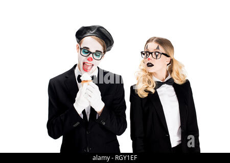 Fröhliche Clown in Anzug und Brille auf leckeren Kuchen in der Nähe von Frau isoliert auf weiss Stockfoto