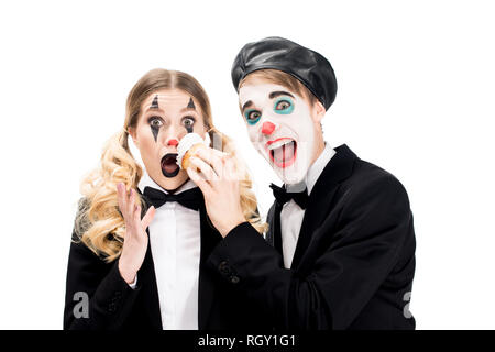 Crazy clown werfen Cupcake im Gesicht der überrascht, Frau isoliert auf weiss Stockfoto