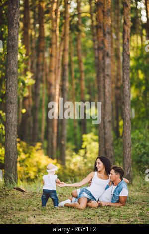 Das Thema Familie Erholung in Forest Park. Junge schöne stilvolle kaukasischen Familie mit kleinem Kind Tochter ein Jahr alt sitzen auf der gr Stockfoto