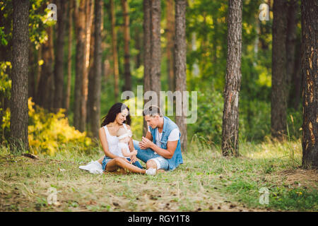 Das Thema Familie Erholung in Forest Park. Junge schöne stilvolle kaukasischen Familie mit kleinem Kind Tochter ein Jahr alt sitzen auf der gr Stockfoto