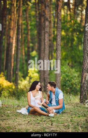 Das Thema Familie Erholung in Forest Park. Junge schöne stilvolle kaukasischen Familie mit kleinem Kind Tochter ein Jahr alt sitzen auf der gr Stockfoto