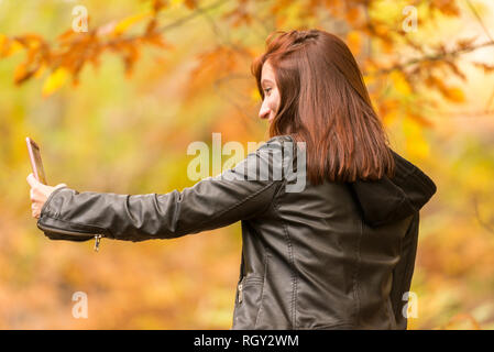Eine junge Frau mit rötlichen Haaren tut selfies mit Ihrem Mobiltelefon im Wald Stockfoto