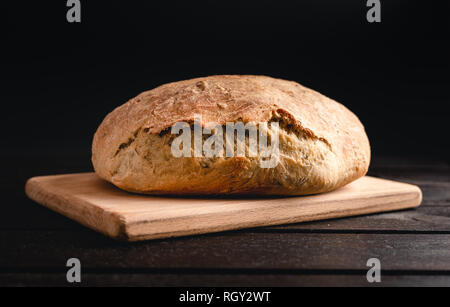 Beleuchtete handgefertigte Brot auf Holz- und schwarzen Hintergrund. Nahaufnahme Foto mit hausgemachtem Brot. Stockfoto