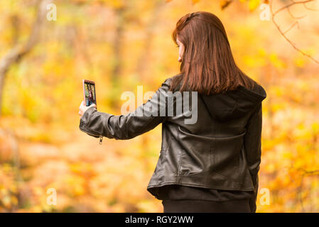 Eine junge Frau mit rötlichen Haaren tut selfies mit Ihrem Mobiltelefon im Wald Stockfoto