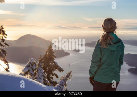 Junge kaukasische Mädchen genießen Sie die herrliche Aussicht auf dem Gipfel eines Berges während eines Winters Sonnenuntergang. Auf Mnt Harvey, in der Nähe von Vancouver, BC, Kanada. Stockfoto