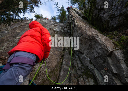 Kletterer sichern, während Ihr Partner Klettern am Rand der Klippe ist. In Area 44 in der Nähe von Squamish und Whistler, nördlich von Vancouver, BC, können Stockfoto