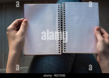 Woman's Hände halten öffnen gesäumt Notebook mit gefütterter Seiten auf dem Schoß Stockfoto