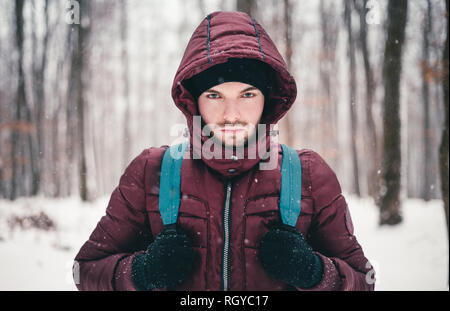 Porträt eines Bergsteigers Mann mit Rucksack im Schnee Blizzard. In der Nähe von Hikerholding sein Rudel in den tiefen und den gefrorenen Wald im Winter. Abenteurer Ich Stockfoto