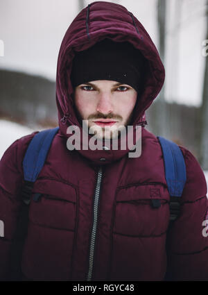 Porträt eines Bergsteigers Mann mit Rucksack im Schnee Blizzard. In der Nähe von Hikerholding sein Rudel in den tiefen und den gefrorenen Wald im Winter. Abenteurer Ich Stockfoto