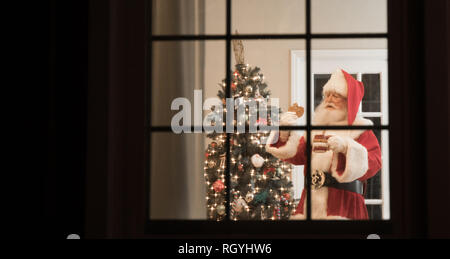 Santa ist durch ein Fenster an Heiligabend essen ein Cookie gesehen. Stockfoto