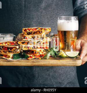 Mann hält auf Schneidebrett Snack für Bier: quesadilla mit Gemüse und Käse mit lagerbier Stockfoto