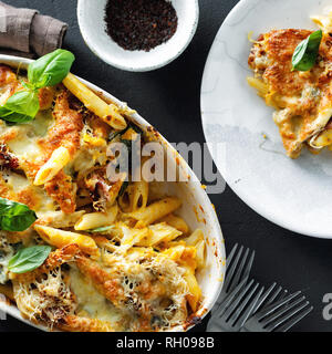 Gebackene Nudeln mit Huhn, Schinken und Mozzarella und Parmesan mit Kürbis Sauce auf dunklem Hintergrund der Ansicht von oben. Komfort Essen Stockfoto