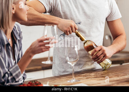 7/8-Ansicht von Freund und Öffnen der Flasche Wein in der Nähe der Freundin Stockfoto