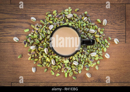 Ein Haufen leckeren Pistazien umgeben einen Becher heißen Kardamom schwarzer Tee. Stockfoto