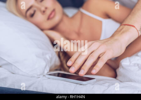 Schuss des Menschen erreichen für Smartphone, während junge Frau schlafen im Bett, Misstrauen Konzept 7/8 Stockfoto