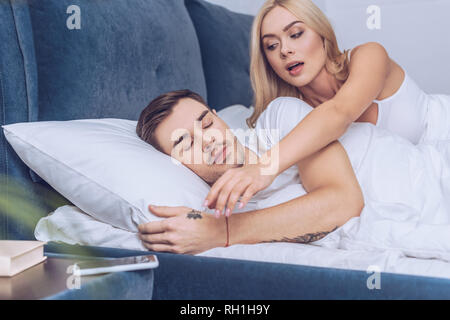 Eifersüchtige Frau erreichen für Smartphone, während Freund schlafen im Bett, Misstrauen Konzept Stockfoto