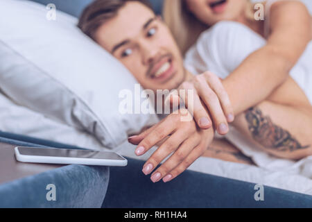 7/8 Schuß von wütenden Mann die Hand der Frau erreichen für Smartphone im Schlafzimmer Stockfoto