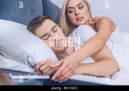 Eifersüchtige Frau erreichen für Smartphone, während Freund schlafen im Bett Stockfoto