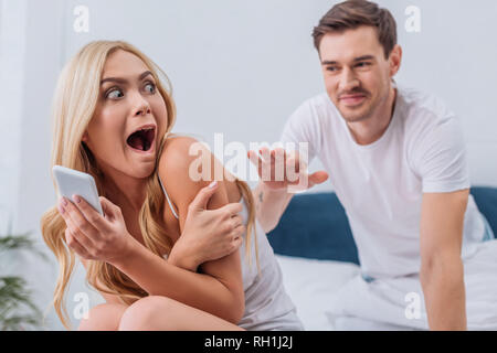 Mann erreichen zu Angst junge Frau mit Smartphone auf dem Bett, Misstrauen Konzept Stockfoto