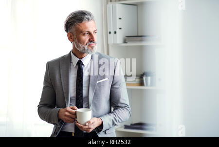 Eine ernsthafte Reife Geschäftsmann in einem Büro, mit einer Tasse Kaffee. Kopieren Sie Platz. Stockfoto