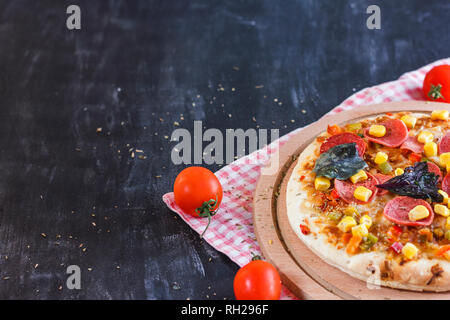 Pizza mit Mais, Würstchen, Tomaten auf Holz- runde Board Stockfoto