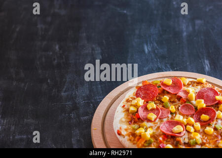 Pizza mit Mais, Würstchen, Tomaten auf Holz- runde Board Stockfoto