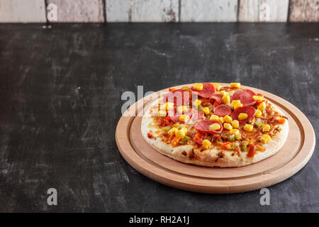 Pizza mit Mais, Würstchen, Tomaten auf Holz- runde Board Stockfoto