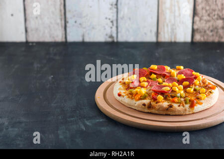 Pizza mit Mais, Würstchen, Tomaten auf Holz- runde Board Stockfoto