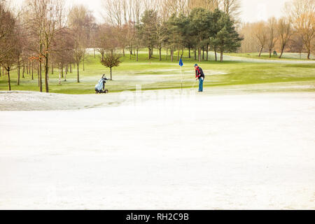 Mann spielt Golf im Winter auf Golf ein Kurs trotz Schnee und eisigen Temperaturen bei Malkins Bank in der Nähe von Sandbach Cheshire England Großbritannien Stockfoto