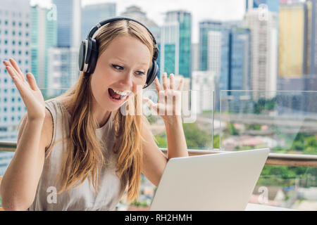 Junge Frau lehrt eine Fremdsprache lernt eine Fremdsprache im Internet auf ihrem Balkon vor dem Hintergrund einer großen Stadt. Online Sprache Stockfoto