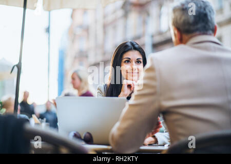 Mann und Frau Geschäftspartner mit Laptop sitzen in einem überfüllten Café in der Stadt, zu sprechen. Stockfoto