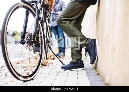 Ein Mittelteil der unkenntlich Active Senior Paar mit elektrobikes stehen draußen auf einer Straße in der Stadt. Stockfoto