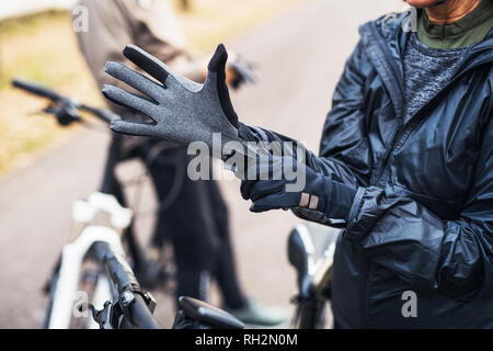 Ein Mittelteil der Active Senior Paar mit elektrobikes stehen draußen auf der Straße, indem auf Handschuhe. Stockfoto