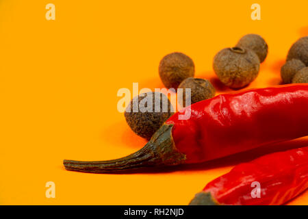 Schließen Sie herauf frische rote Chili und Ganze schwarzer Pfeffer auf eine goldene Farbe Hintergrund, Low Angle Seitenansicht Stockfoto