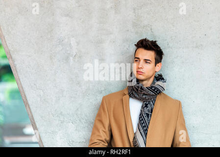 Vorderansicht des stilvollen jungen Mann mit Mantel und Schal, lehnte sich an die Wand, während Sie auf der Suche Stockfoto