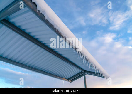 Schneebedecktes Dach mit Eiszapfen gegen bewölkt blauer Himmel Stockfoto