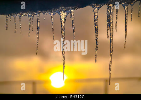 Transparente Eiszapfen vom Dach bei Sonnenuntergang hängen Stockfoto